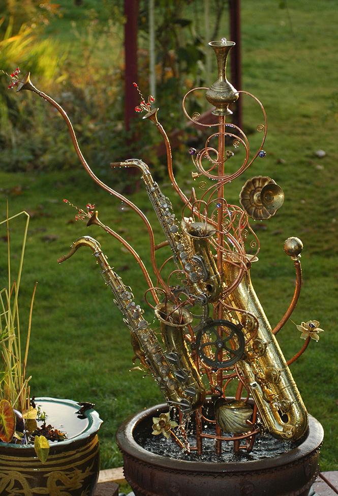 Musical instrument fountain sculpture made from copper tubing, a water wheel, repurposed brass and glass, and upcycled musical instruments including an alto sax, a tenor sax, and a baritone sax. 